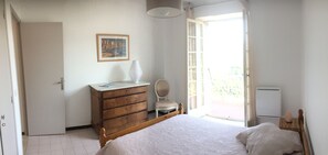 Quarto com cama, penteadeira, cadeira, radiador e janela com vista.