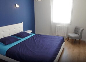 A bedroom with a bed, a chair, a window, and a radiator.