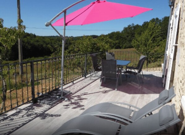 A patio with a table and chairs, a pink umbrella, and a view of a vineyard.