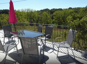 A balcony with a table and chairs, a red umbrella, and a view of a green landscape. - GITE JASMIN (Notre-Dame-de-Sanilhac)