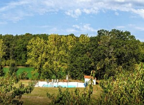 A rural landscape with a small building, possibly a house or a barn, surrounded by dense trees and a clear sky.
