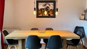A dining area with a wooden table, six chairs, and a hanging light fixture above.