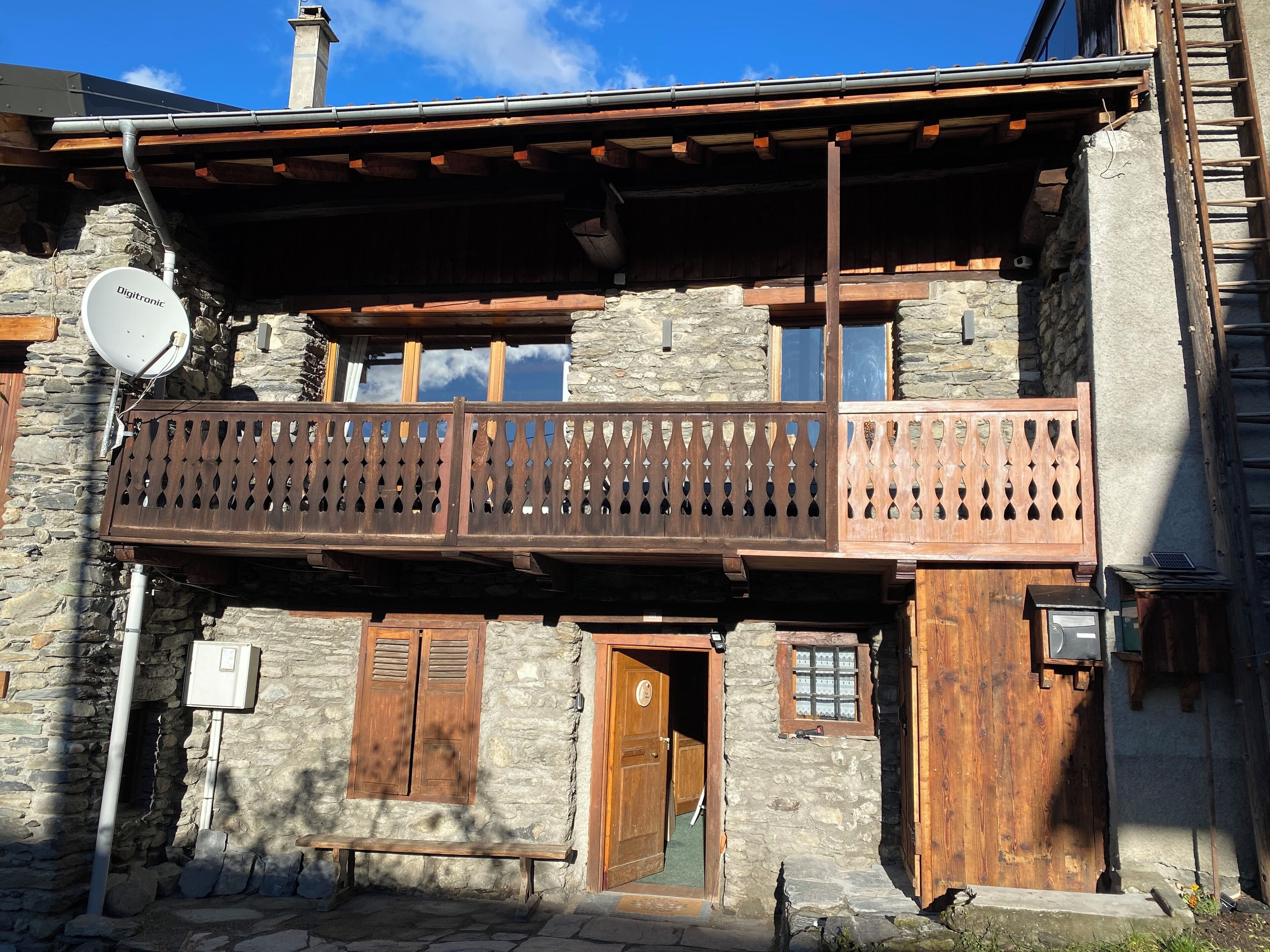 Ein traditionelles Steinhaus mit einem hölzernen Balkon, Steinmauern und einer Satellitenschüssel.