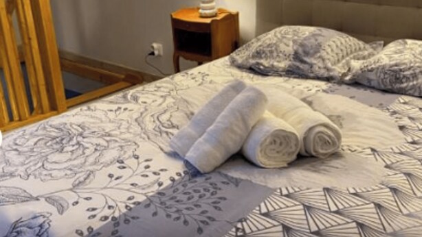 A bed with floral bedding, a headboard, and rolled towels.