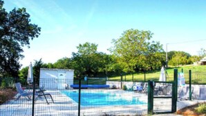 A fenced swimming pool with lounge chairs and a small building, surrounded by greenery.