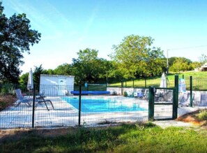 A swimming pool with a net enclosure, lounge chairs, and a small building.