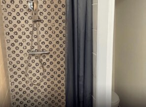 A shower with a floral pattern, a curtain, and a toilet.