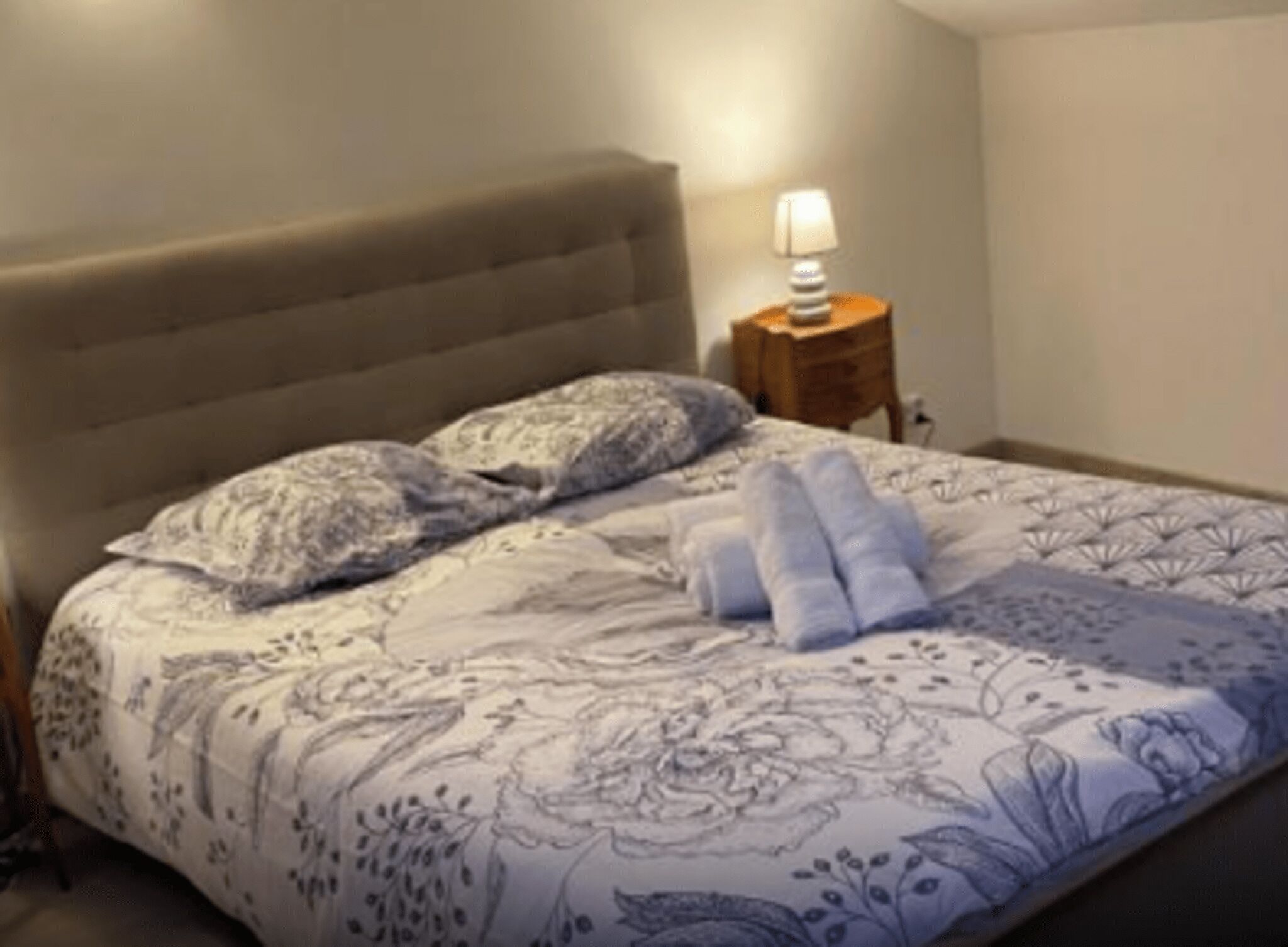 Una cama bien hecha con una colcha de estampado floral, un cabecero y una lámpara de noche.