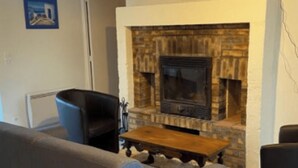 A living room with a stone fireplace, a blue armchair, and a wooden coffee table.