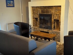 A living room with a stone fireplace, a blue armchair, and a wooden coffee table.