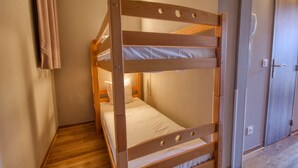 Un lit superposé dans une pièce dont le sol est en bois, avec une porte et un luminaire fixé au mur.