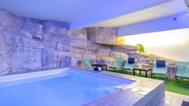 Une piscine bordée d’un muret en pierre, avec des chaises longues et une petite table.