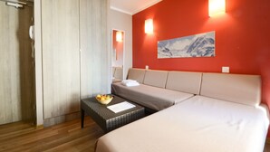 Une chambre d’hôtel avec un lit, un canapé, une petite table avec des fruits, une lampe fixée au mur et un tableau.