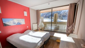Une chambre d’hôtel avec un lit, une chaise, une table, une vue sur une montagne enneigée et un mur rouge.