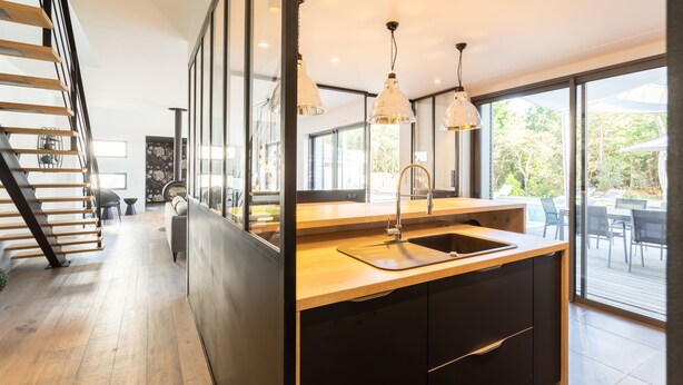 Une cuisine moderne dotée d’un plan de travail en bois, d’un évier en acier inoxydable et de luminaires suspendus.