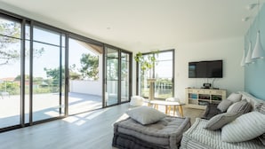 Un salon moderne avec un canapé, un téléviseur et une porte-fenêtre coulissante donnant sur un balcon.