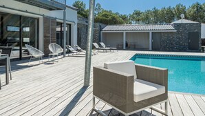 Une terrasse en bois avec une piscine, des chaises longues et un espace salon abrité.