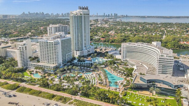 A high-rise hotel with multiple floors, a swimming pool, and a beach area.