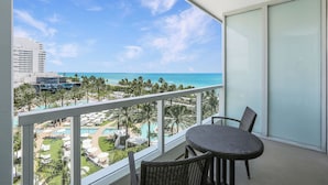 A balcony with a view of a resort pool, palm trees, and a beach.