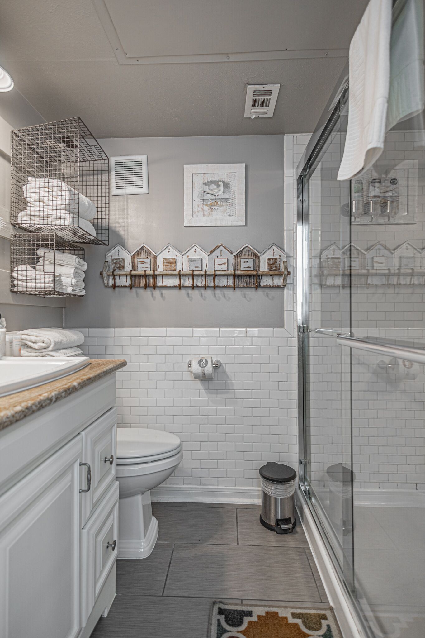 A bathroom with a toilet, a sink with a towel rack, a shower, and a trash can.