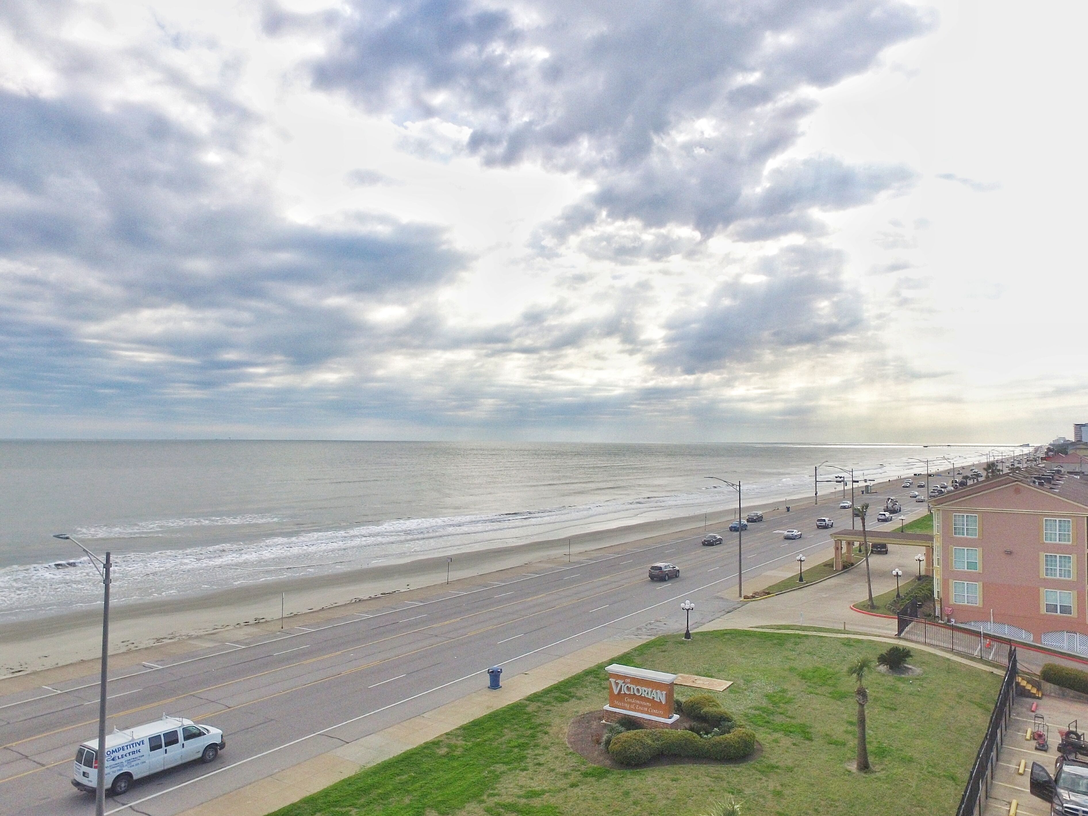 A coastal road with a beach view, a parking lot, and a building with a sign.