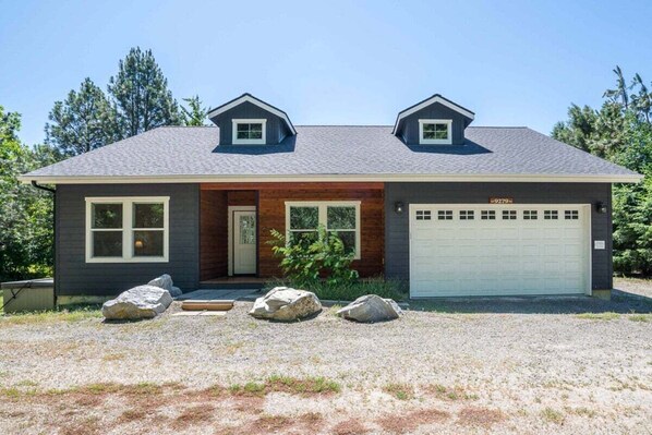 A two-story house with a garage, a front porch with a wooden door, and a gravel driveway.
