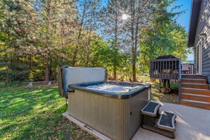 A hot tub in a backyard with a wooden deck and stairs leading to a porch.