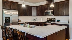 Uma cozinha moderna com armários de madeira escura, eletrodomésticos de aço inoxidável e iluminação pendente.