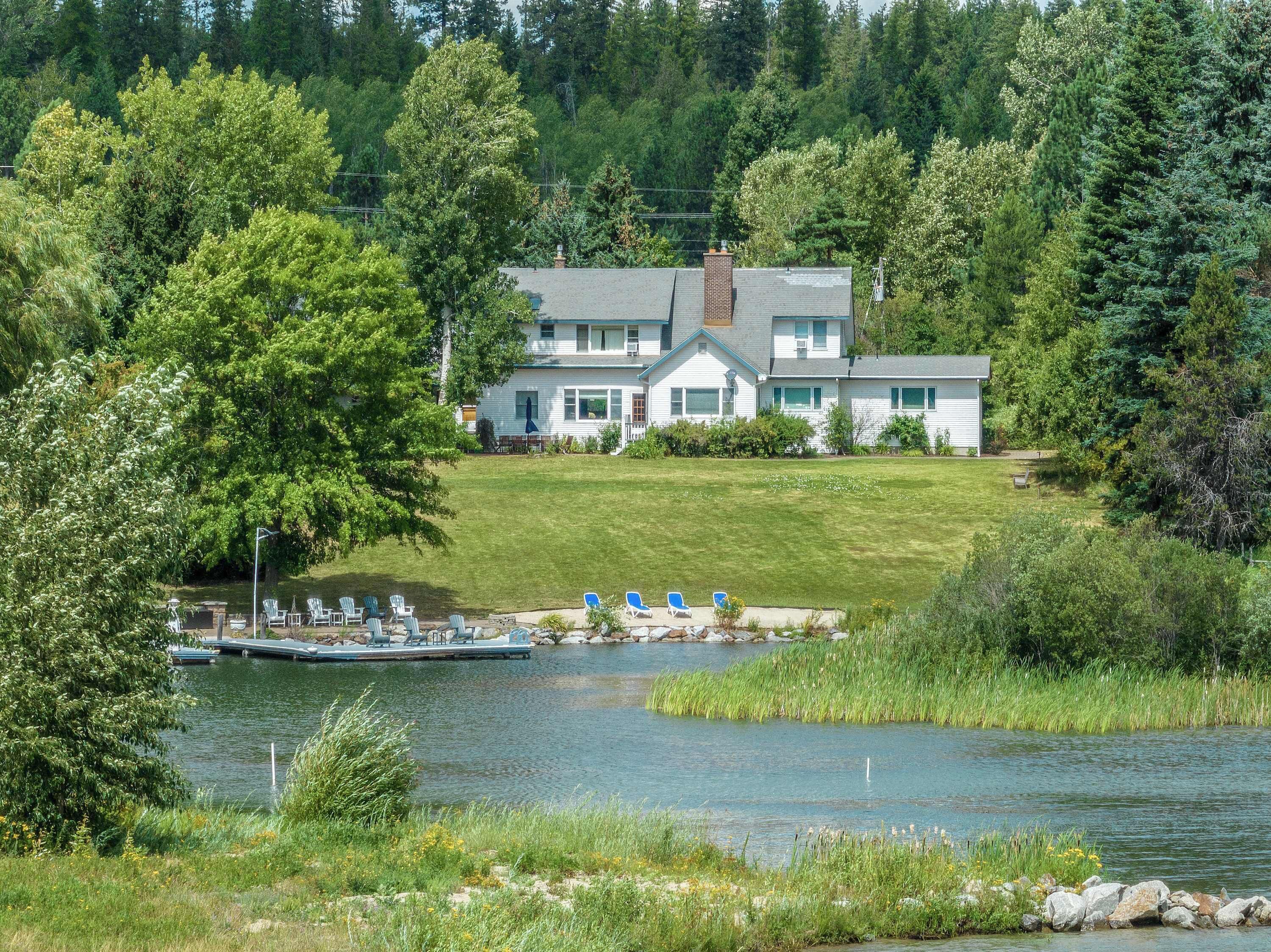 A lakeside house with a dock, surrounded by lush greenery and trees.