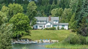 Una casa frente al lago con un muelle, rodeada de exuberante vegetación y árboles.
