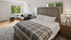Un dormitorio con una cama grande, una mesita de noche, una lámpara, un sofá y una ventana con vistas a zonas verdes.