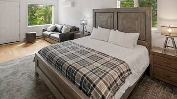 Une chambre à coucher avec un grand lit, une table de chevet, une lampe, un canapé et une fenêtre donnant sur un paysage verdoyant.