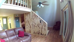 A spacious living area with a brown leather sofa, a wooden staircase, and a ceiling fan.