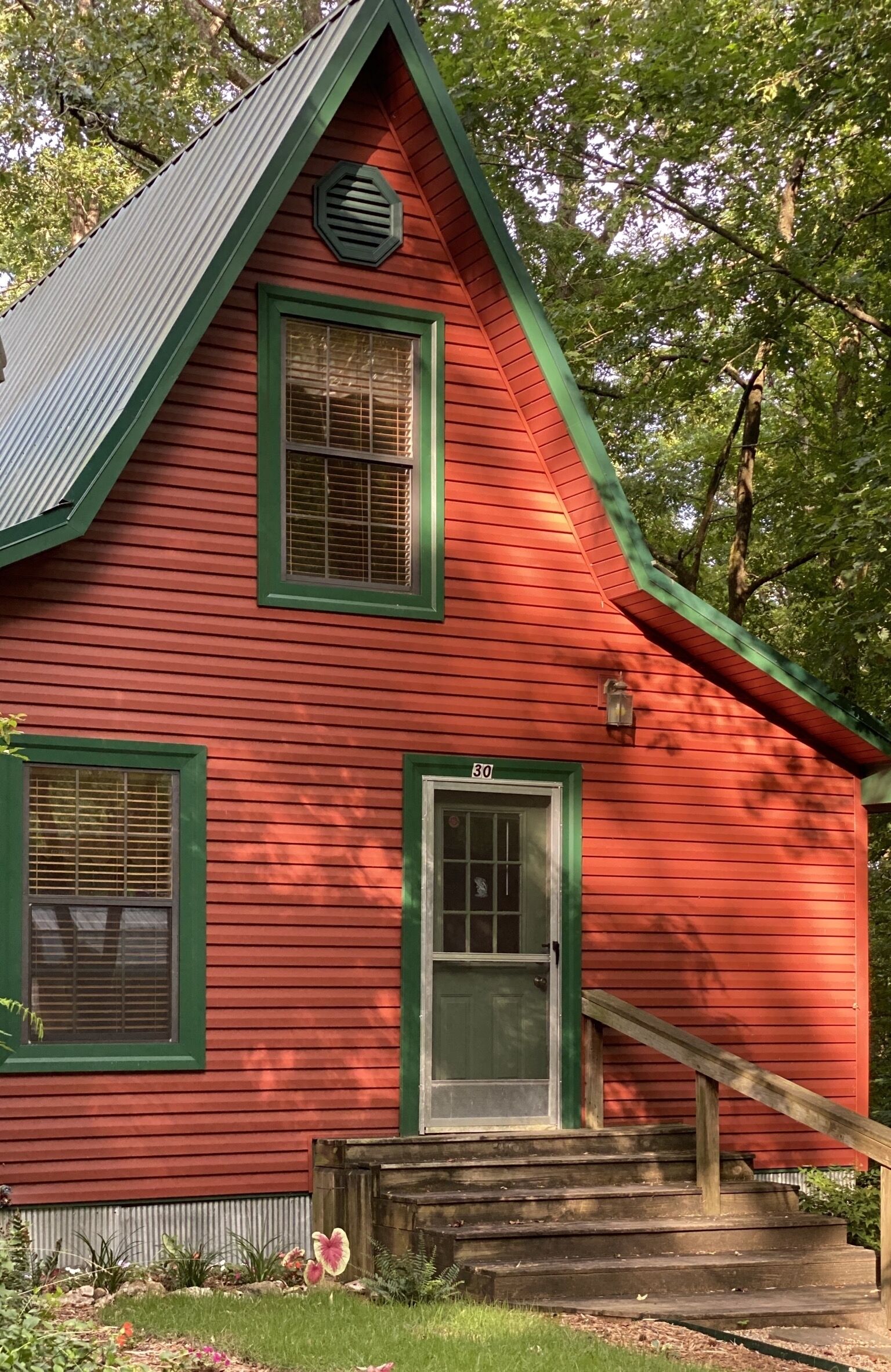 Una casa de madera roja con detalles verdes, el número '30' en la puerta y un pequeño porche con escalones.