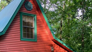 A red wooden house with a green roof, a front door, and a small porch with steps.