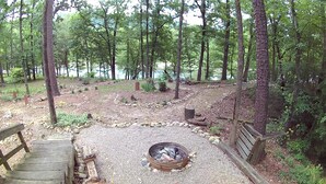 A campsite with a fire pit, wooden benches, and a gravel area surrounded by trees.