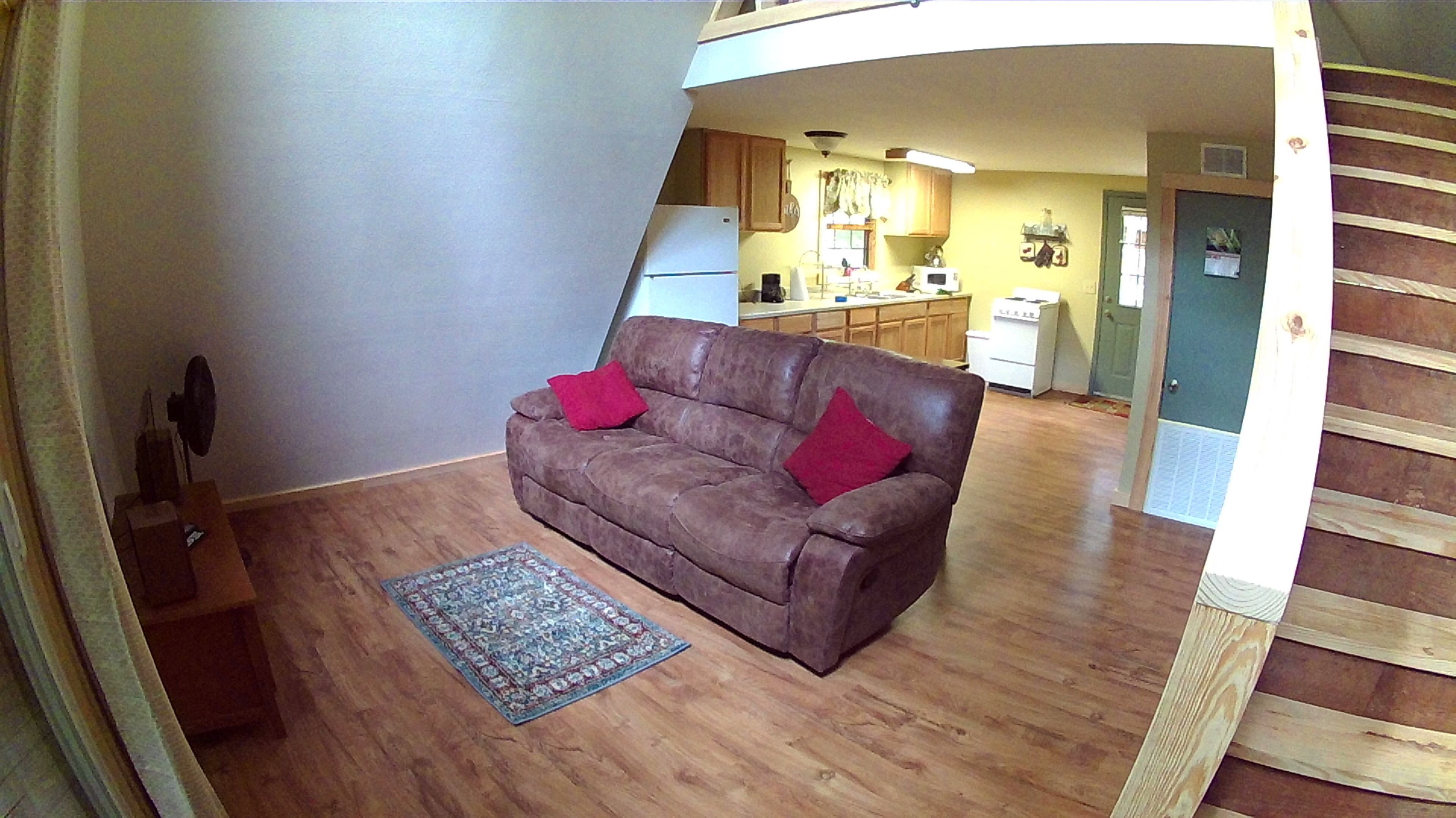 Ein Wohnzimmer mit einer braunen Ledersofa, zwei roten Kissen und einem blau gemusterten Teppich.