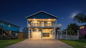 A two-story house with a balcony, a garage, and a well-lit driveway at night. - Beach Cottage with Soaking Pool & Outdoor Oasis (Galveston)