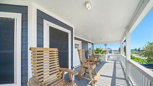 A wooden deck with several wooden chairs and a bench, a white railing, and a view of the ocean. - Beach Cottage with Soaking Pool & Outdoor Oasis (Galveston)