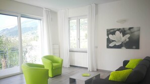 A modern living room with a large window, two green chairs, a grey sofa with a bright green pillow, and a small coffee table. - Single house, 2 double and 1 single room A/C and wifi "La Svolta Holidays" (Malcesine)