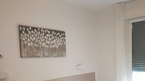 A neatly made bed with white linens, a headboard, a bedside table, a power outlet, a wall-mounted light switch, and a painting of flowers. - Single house, 2 double and 1 single room A/C and wifi "La Svolta Holidays" (Malcesine)