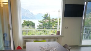 A room with a table, chairs, a radiator, a window with a view of mountains, and a TV on the wall. - Single house, 2 double and 1 single room A/C and wifi "La Svolta Holidays" (Malcesine)
