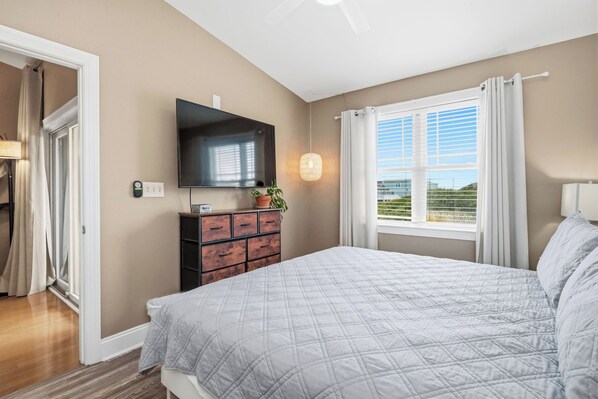 Un dormitorio con cama, cómoda, televisor y ventana con cortinas.