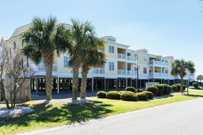 Un hotel de varios pisos con balcones, palmeras y un césped cuidado.