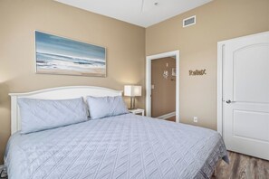 A bedroom with a bed, a nightstand, a lamp, a door, and a wall-mounted artwork.