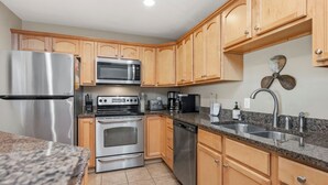 Cocina con gabinetes de madera, electrodomésticos de acero inoxidable, incluyendo un refrigerador, microondas, horno y lavavajillas, encimera de granito y un lavamanos con grifo moderno.
