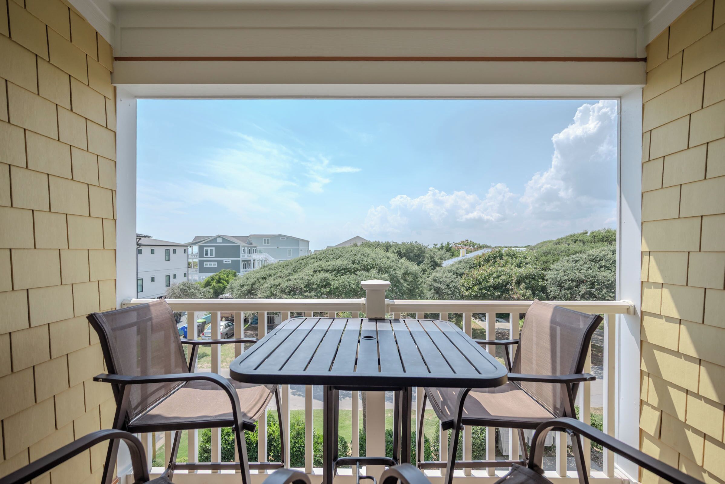 Een balkon met een tafel en stoelen, uitkijkend op een woonwijk met huizen en groen.