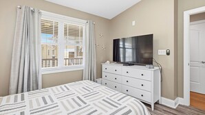Un dormitorio con cama, cómoda, televisor y ventana con cortinas.