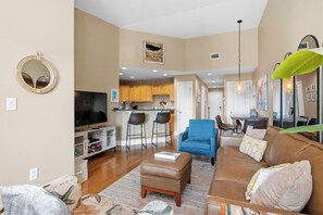 A living room with a brown sofa, blue chairs, and a TV. - Greyt Escape: Lovely, Ocean View Condo Across from OKI Pier with Community Pool, (Oak Island)