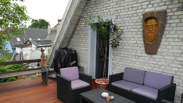 Una terraza en la azotea con mobiliario de mimbre, una parrilla y una talla de madera decorativa.